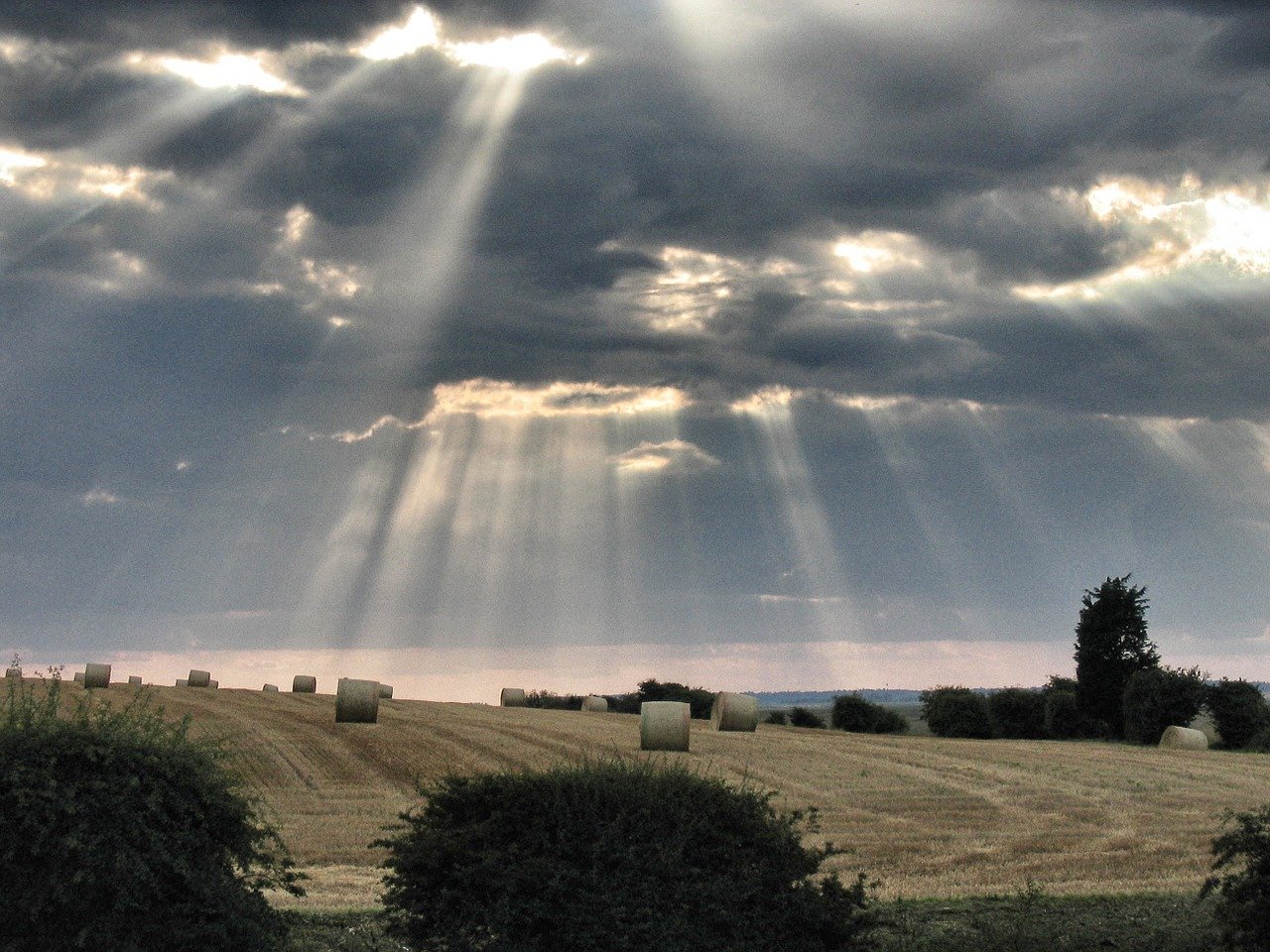 shafts of sunlight over field poking through clouds